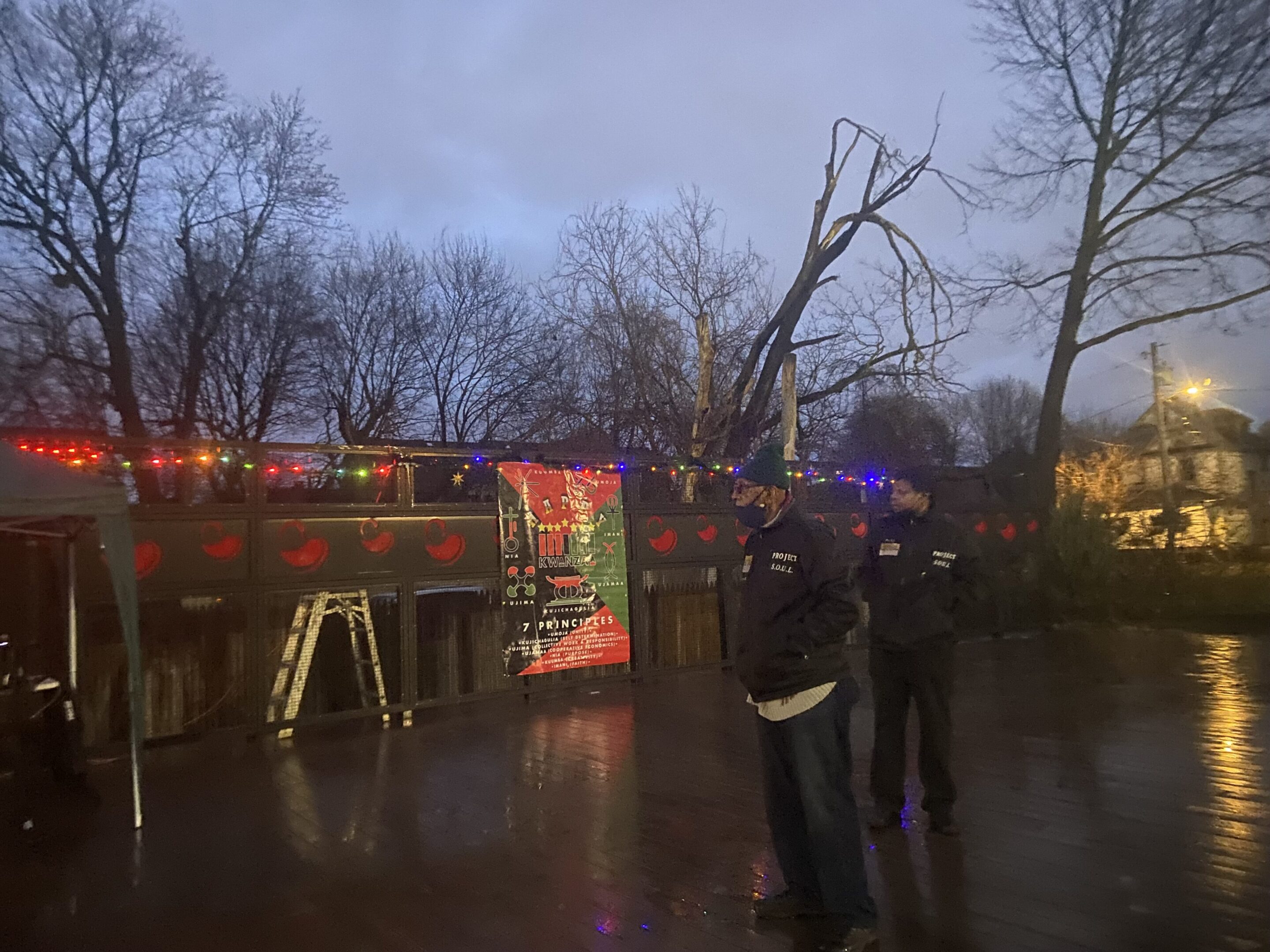 Two people standing near a bus on a rainy evening with colorful lights.