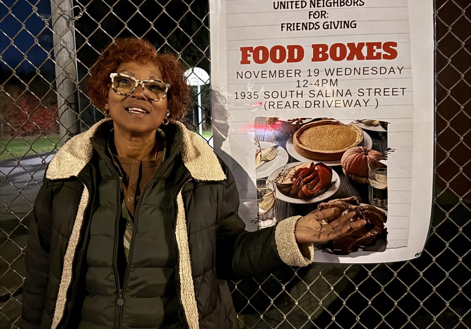 A woman stands next to a sign about food boxes at night.